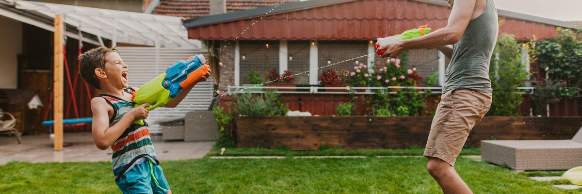 Man and child play with squirt guns in home's yard.