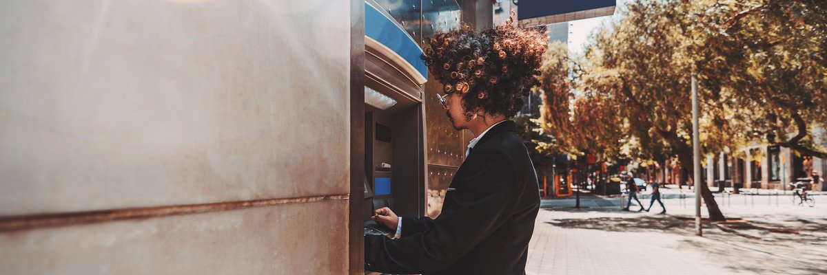 A young man in a suit using an outdoor ATM.