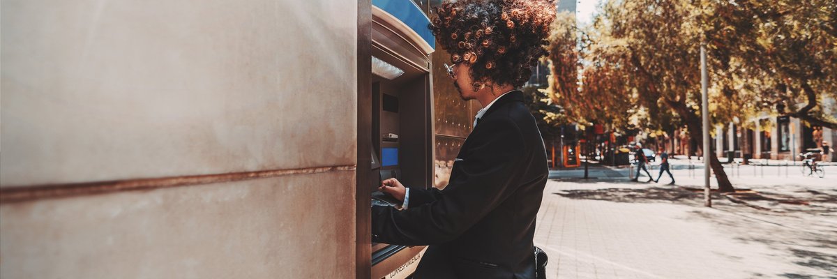 A young man in a suit using an outdoor ATM.
