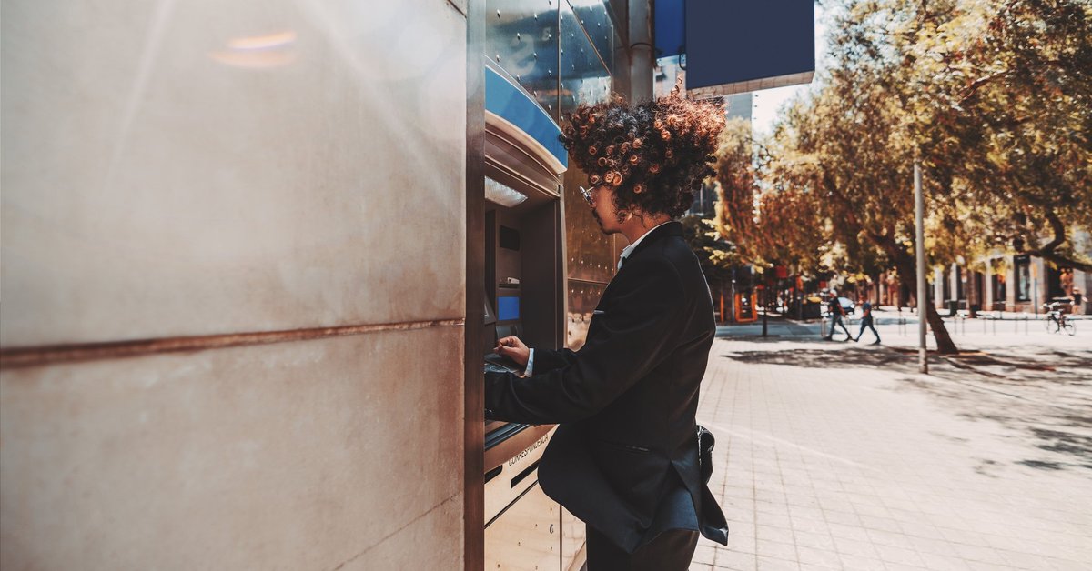 A young man in a suit using an outdoor ATM.