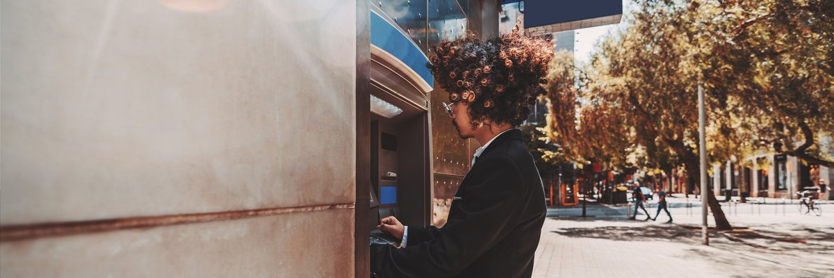 A young man in a suit using an outdoor ATM.