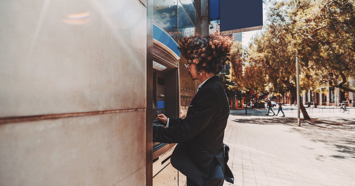 A young man in a suit using an outdoor ATM.