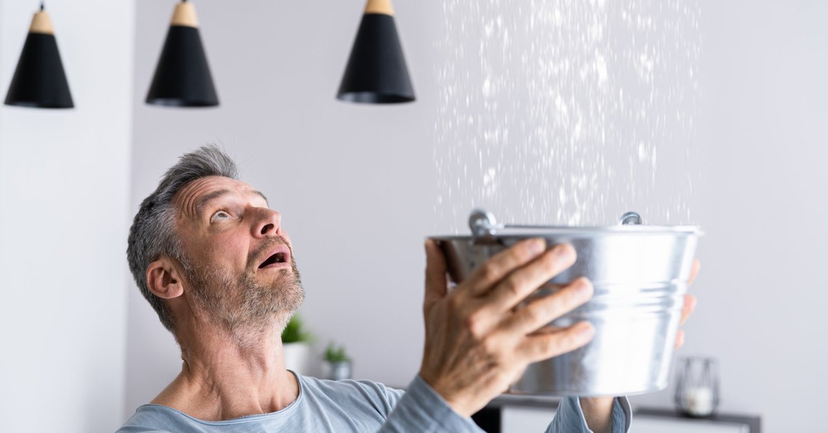Man catching leaking water from ceiling in a bucket.