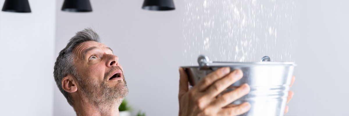 Man catching leaking water from ceiling in a bucket.