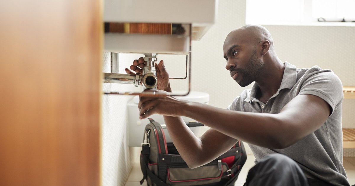 A male plumber fixing the pipes under a sink.