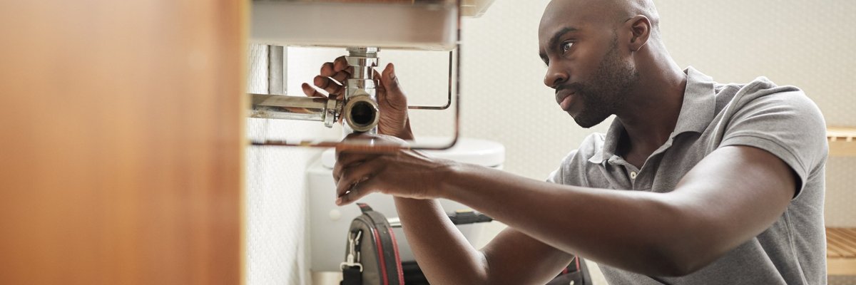 A male plumber fixing the pipes under a sink.