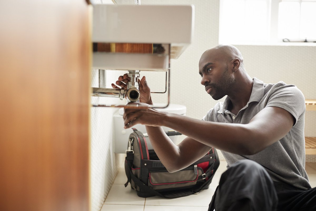 A male plumber fixing the pipes under a sink.