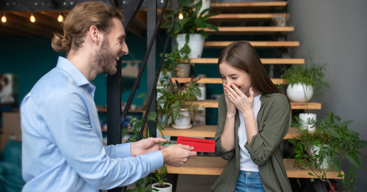 Man hands young girl a gift in an envelope.