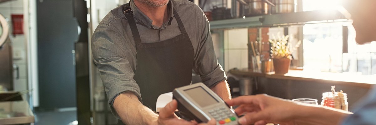 A cafe employee holding a credit card reader while the customer enters their PIN.