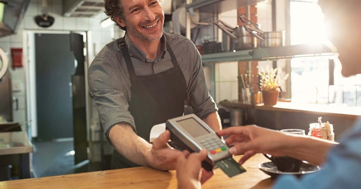 A cafe employee holding a credit card reader while the customer enters their PIN.