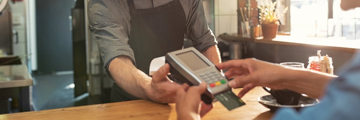 A man behind a counter holding a credit card reader.