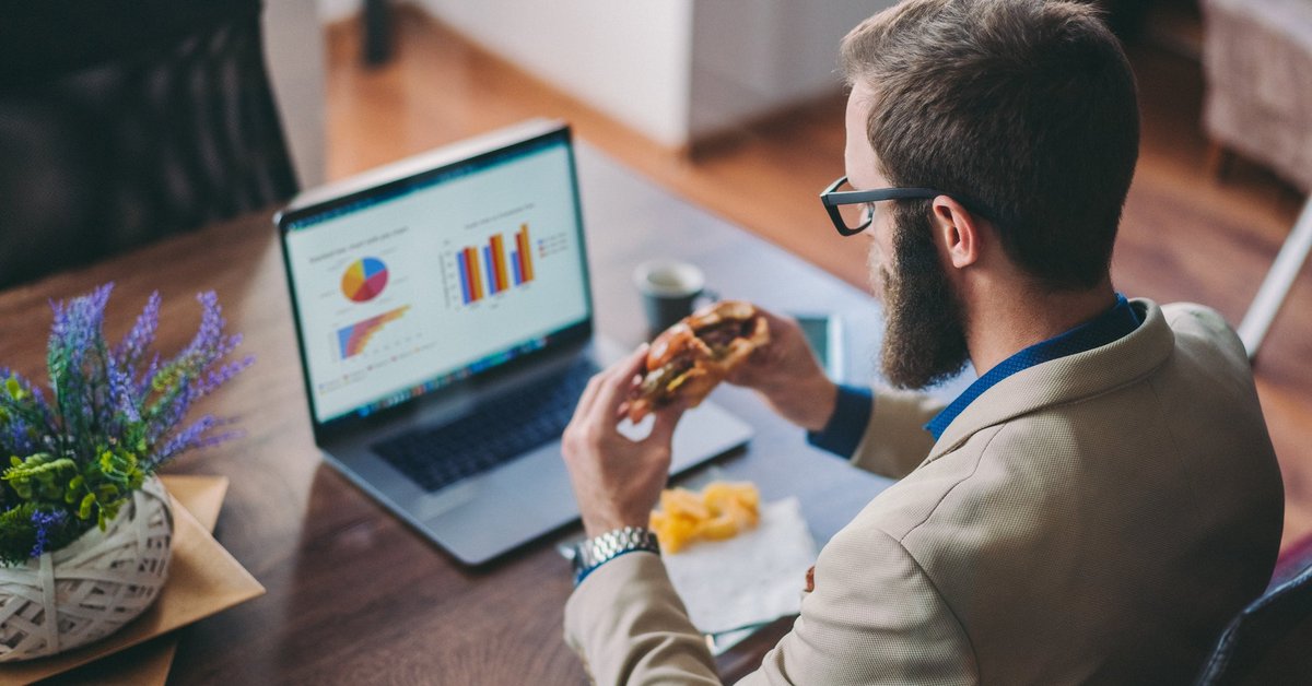 Man in front of laptop eating a burger