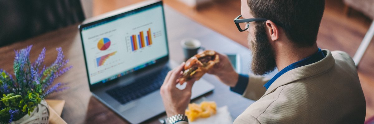 Man in front of laptop eating a burger