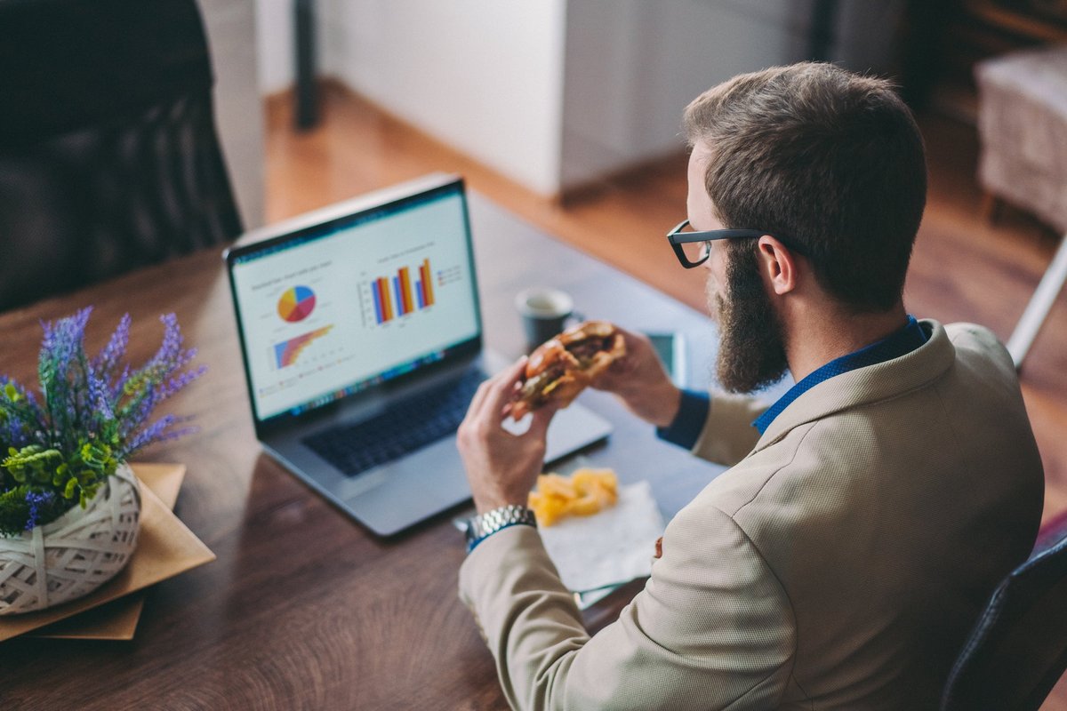 Man in front of laptop eating a burger