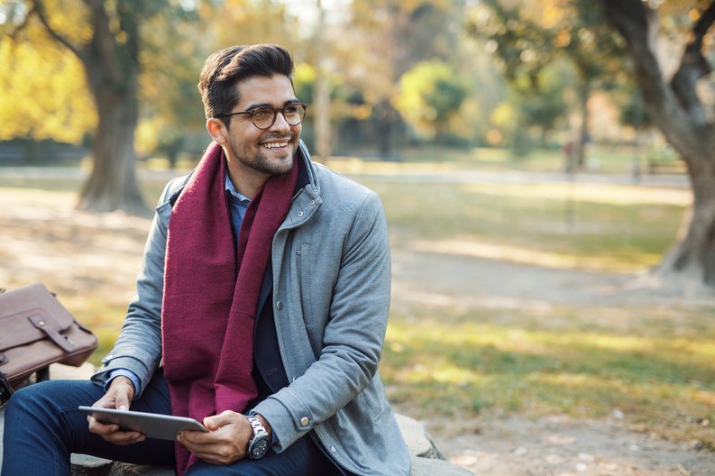 A man sitting on a park bench holding a tablet.