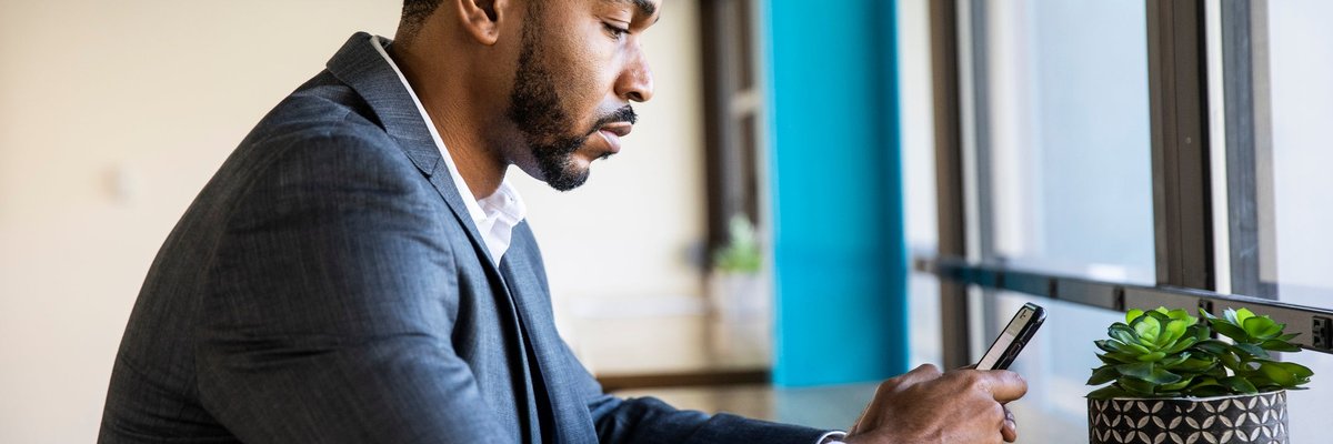 A man in a suit sits and checks his phone.