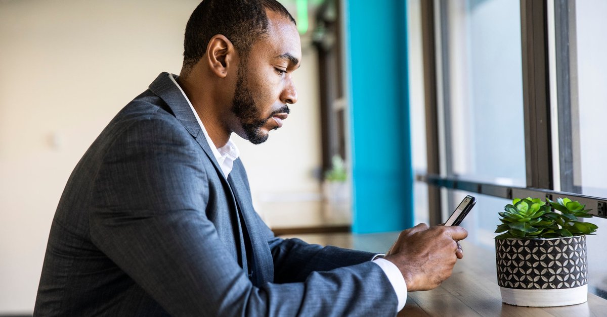A man in a suit sits and checks his phone.