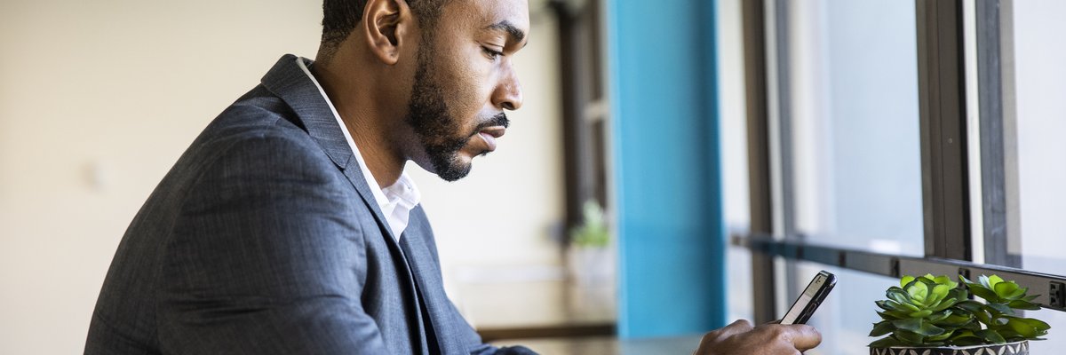 A man in a suit sits and checks his phone.