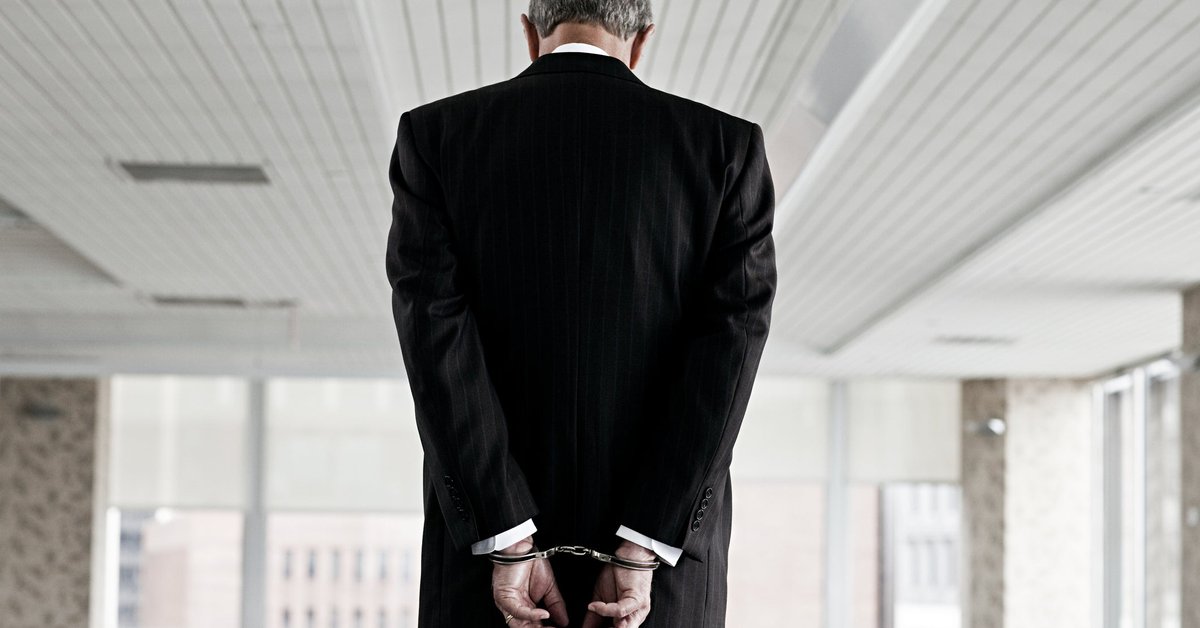 Man in suit with back turned and his hands in handcuffs.