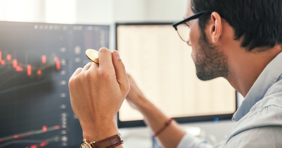 Man looking at charts on a computer screen while holding gold Bitcoin.