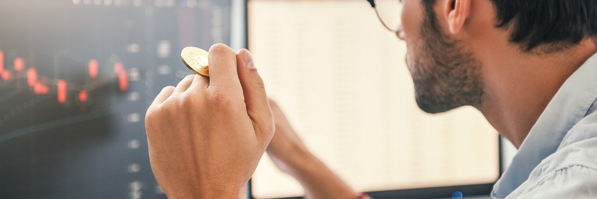 Man looking at charts on a computer screen while holding gold Bitcoin.