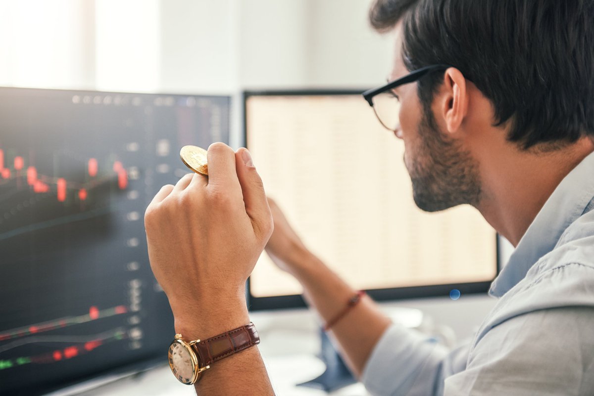 Man looking at charts on a computer screen while holding gold Bitcoin.