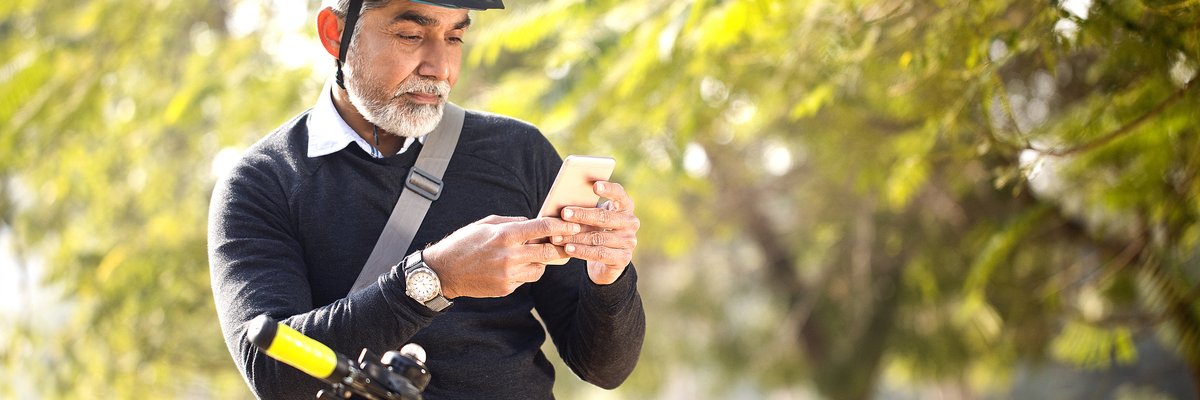 Man looking at his cell phone while riding his bike outdoors among trees.