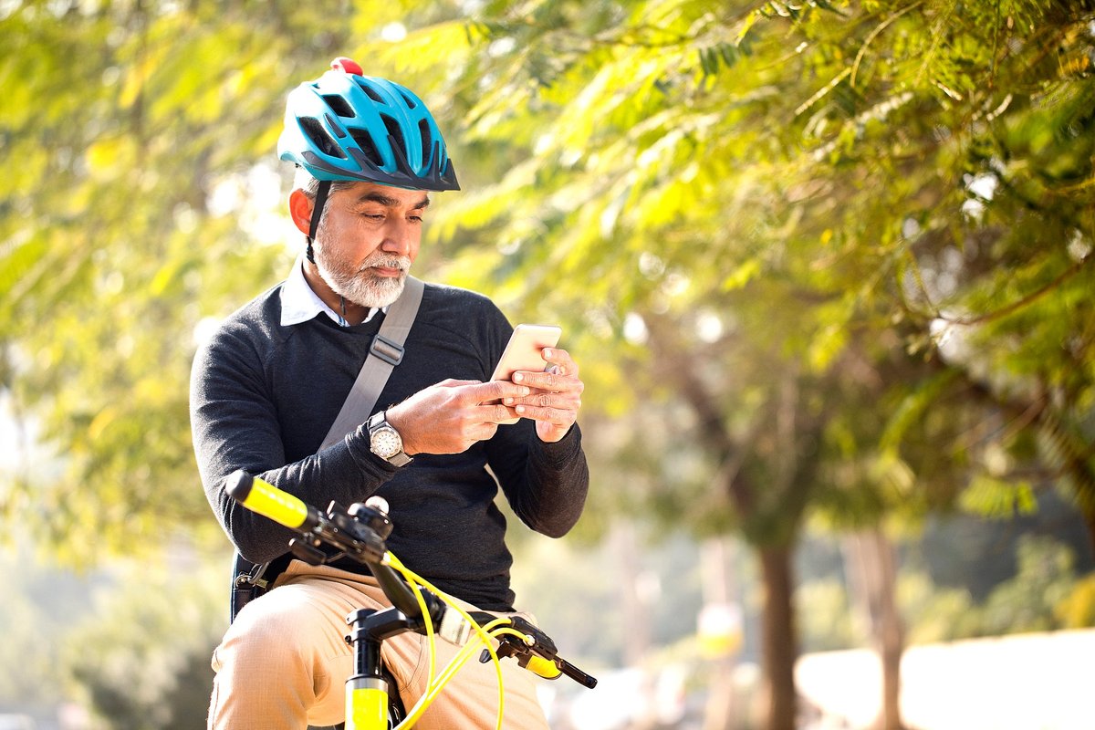 De man kijkt naar zijn mobiele telefoon terwijl hij buiten tussen de bomen fietst.