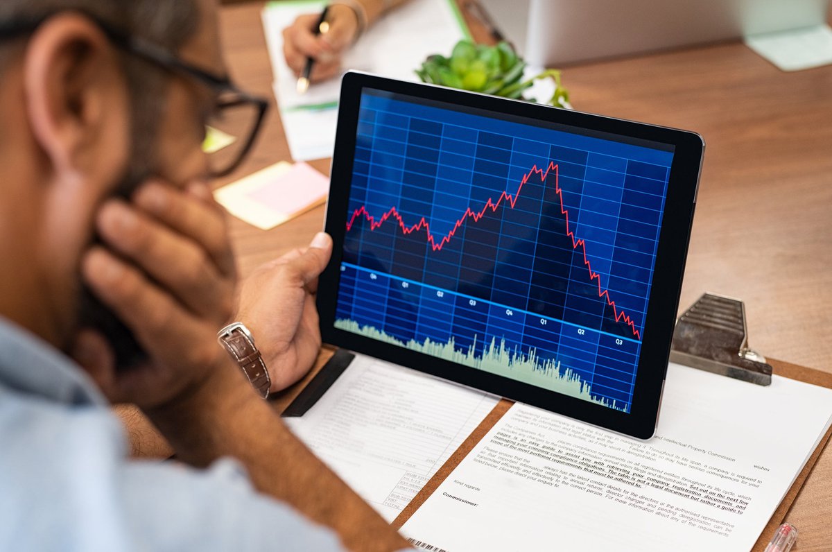 Man looking at tablet with downward trending line graph on it.