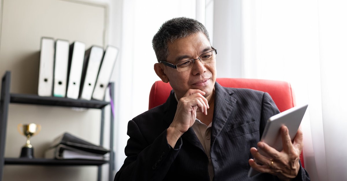 A man sits and looks thoughtfully at his tablet.