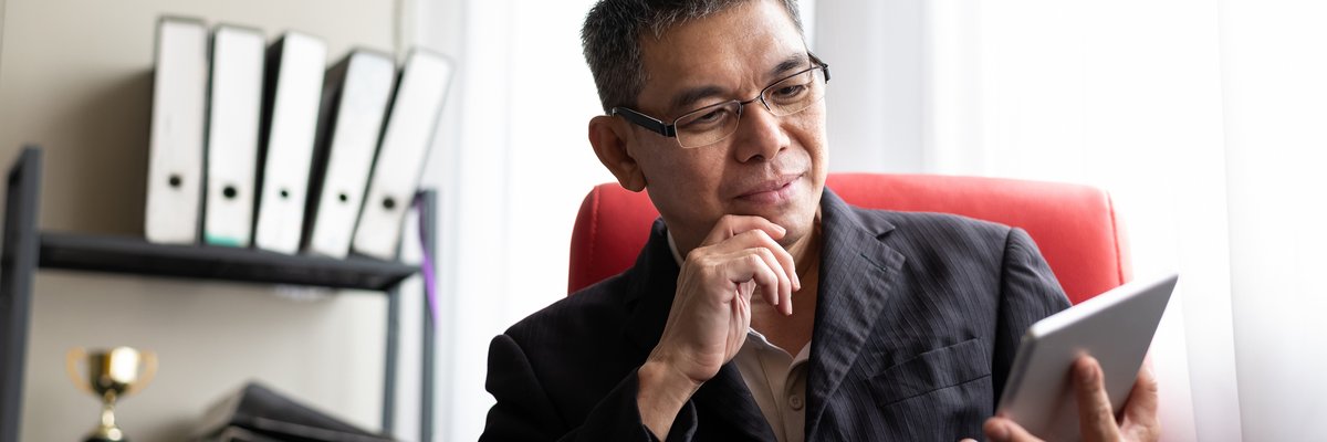 A man sits and looks thoughtfully at his tablet.