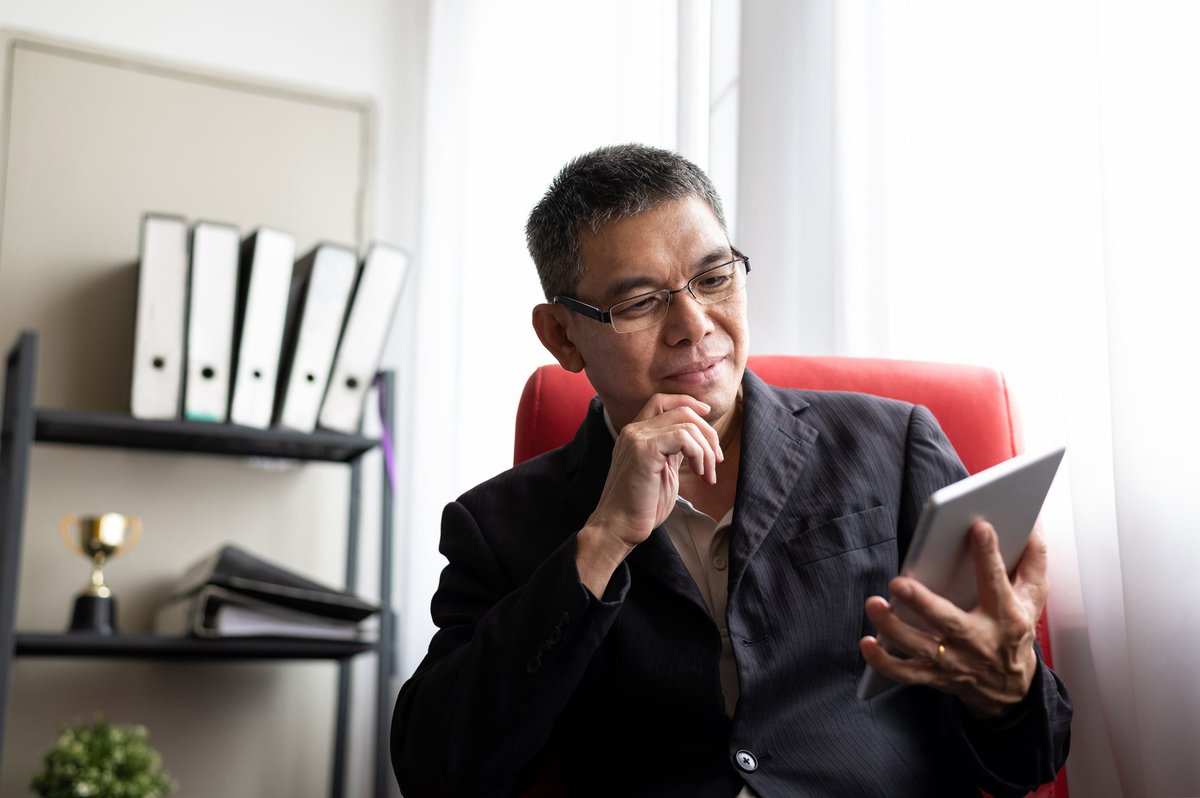 A man sits and looks thoughtfully at his tablet.