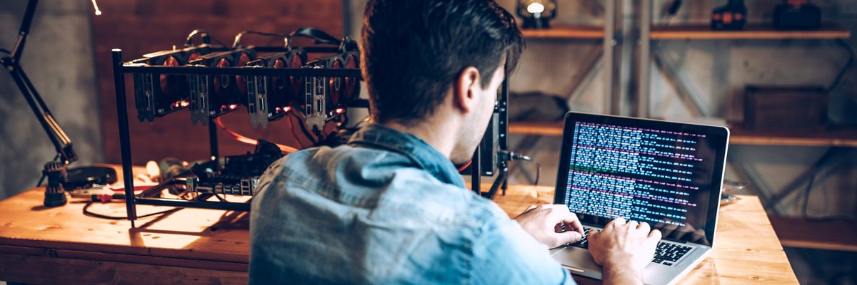 A young adult man mining Bitcoin using his laptop and several hard drives.