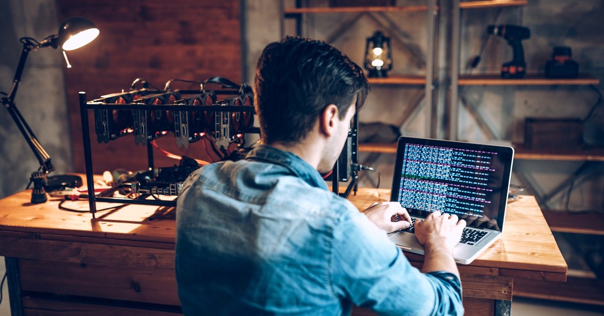 A young adult man mining Bitcoin using his laptop and several hard drives.