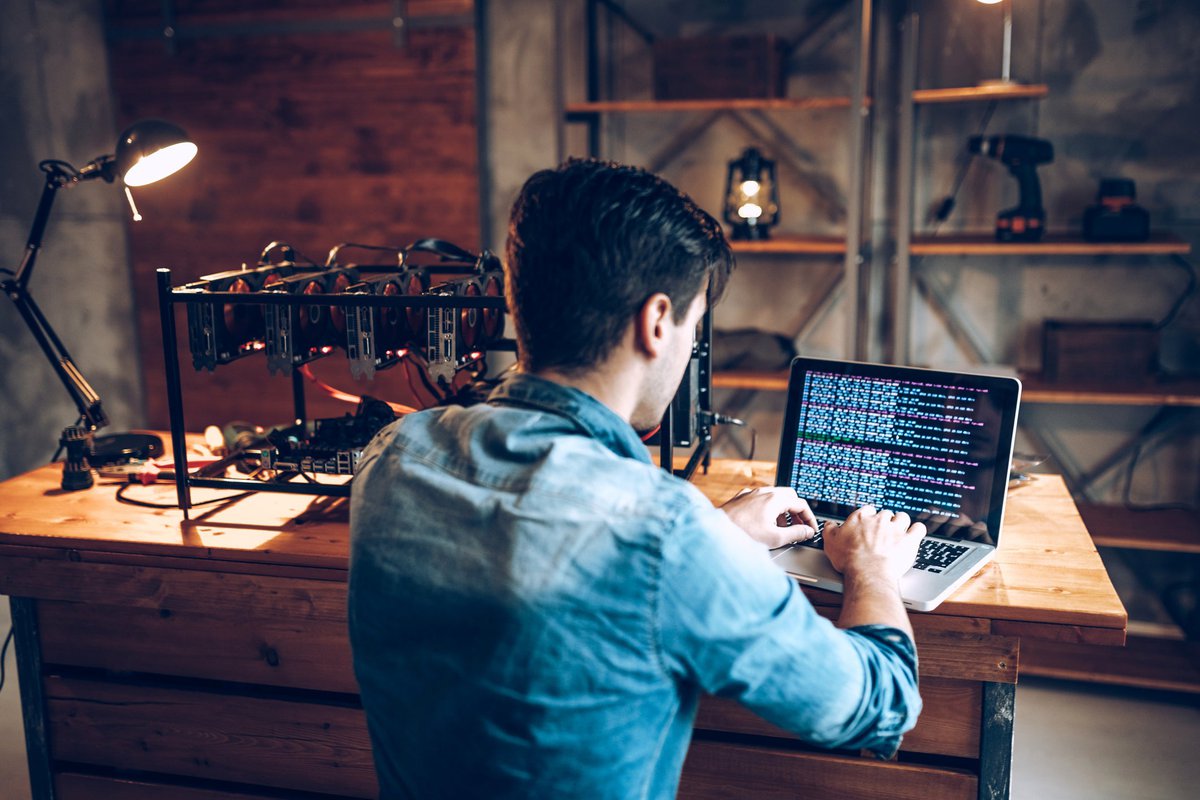 A young adult man mining Bitcoin using his laptop and several hard drives.