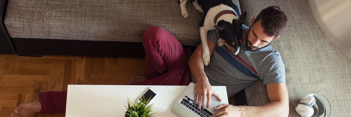 A young man sitting on a couch with his dog and a laptop.