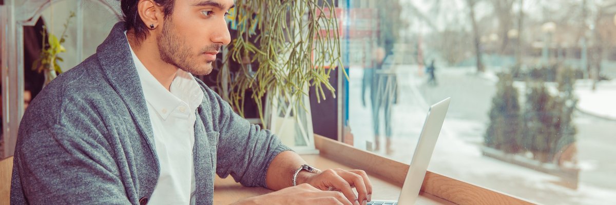 A man working on a laptop while sitting at a window table.