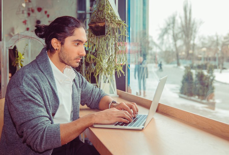 A man working on a laptop while sitting at a window table.