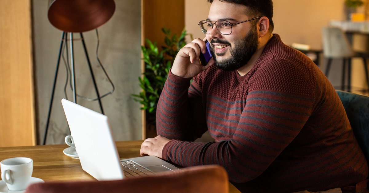 A man talking on the phone while sitting in front of his laptop at a coffeeshop.