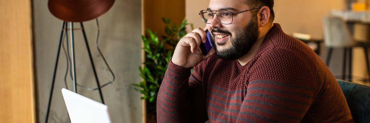 A man talking on the phone while sitting in front of his laptop at a coffeeshop.