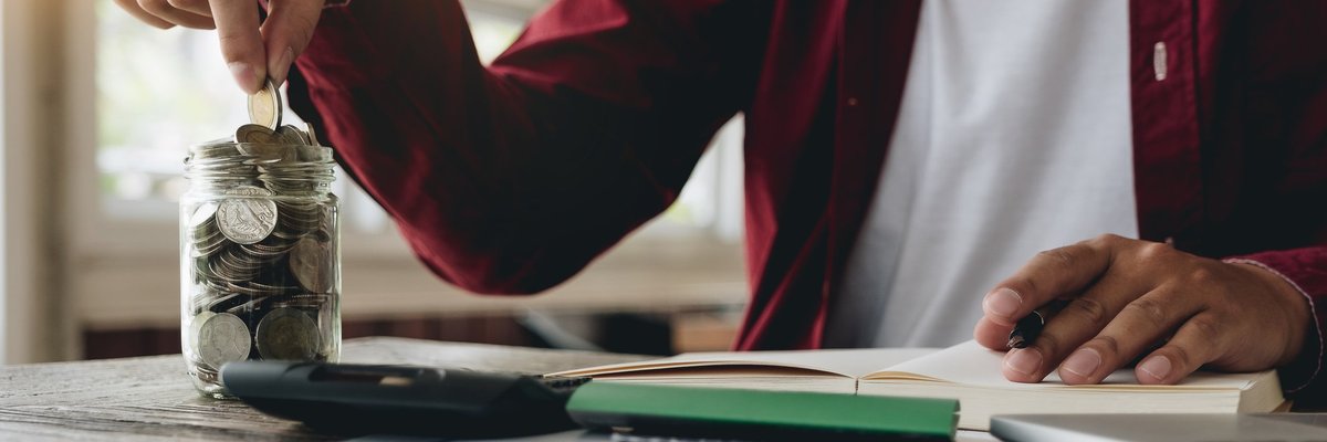 A man putting coins in a jar and doing calculations in a notebook.