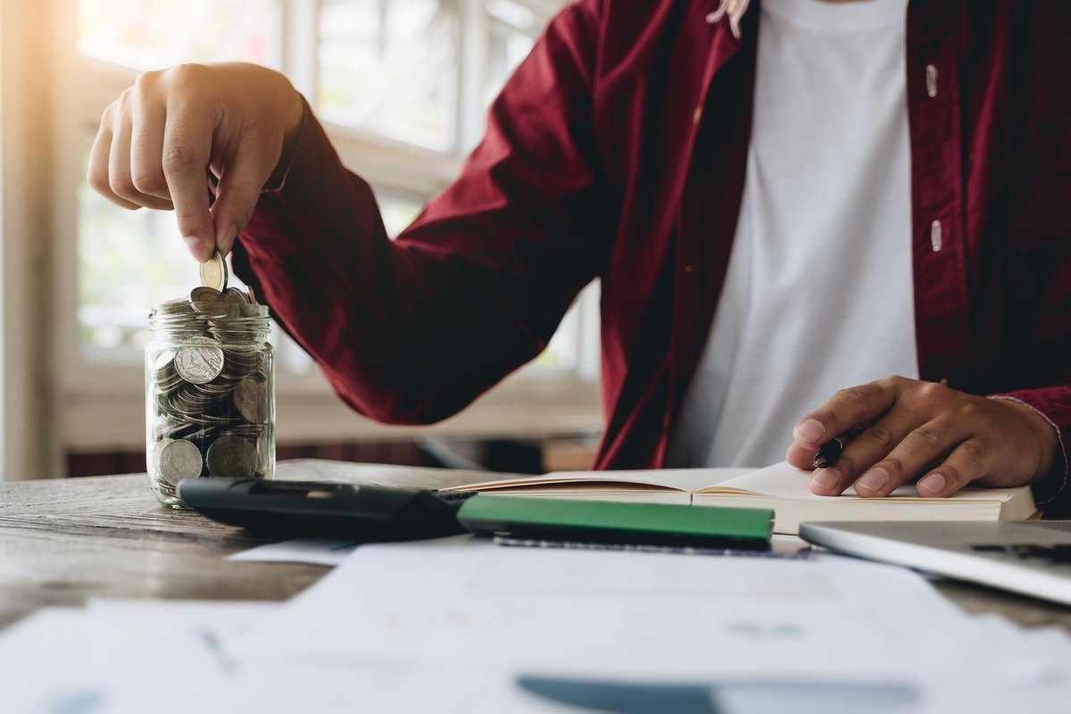 A man putting coins in a jar and doing calculations in a notebook.
