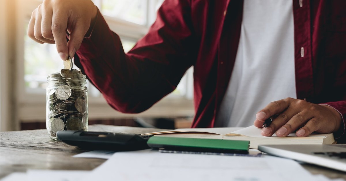 A man putting coins in a jar and doing calculations in a notebook.