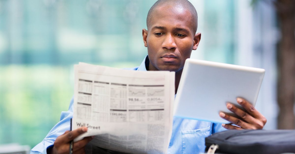 Man reading newspaper and looking at a tablet
