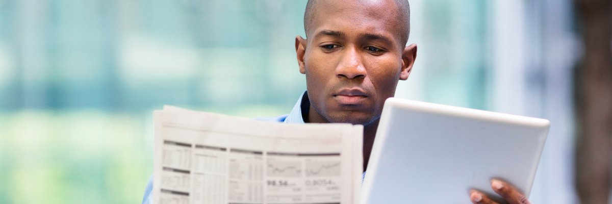Man reading newspaper and looking at a tablet