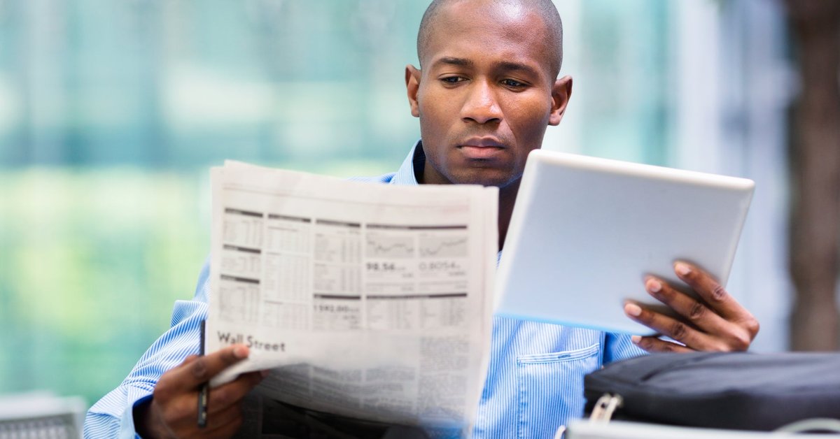 Man reading newspaper and looking at a tablet