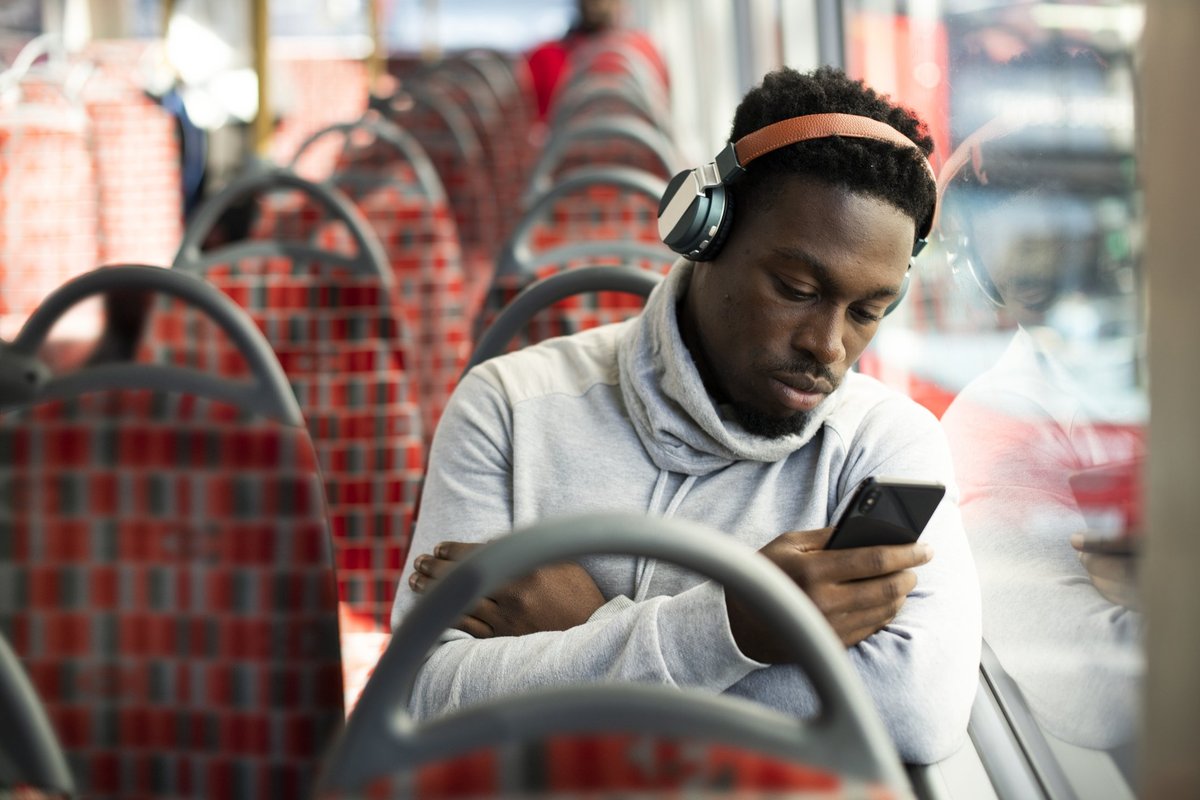 A man on the bus and listening to music while looking at his phone.