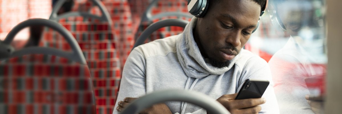 A man riding the bus and listening to music while looking at his phone.