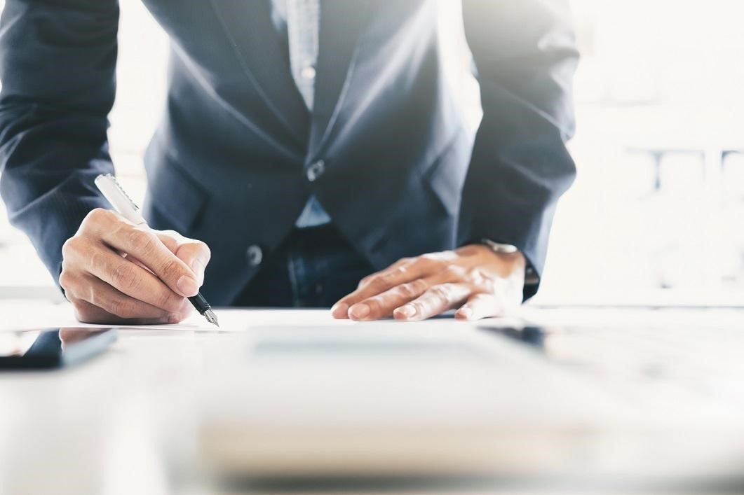 Man in suit signing paperwork on desk.