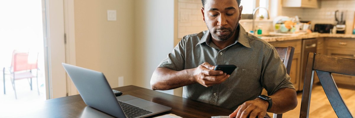 Man sits at counter with phone on laptop utilizing online banking.